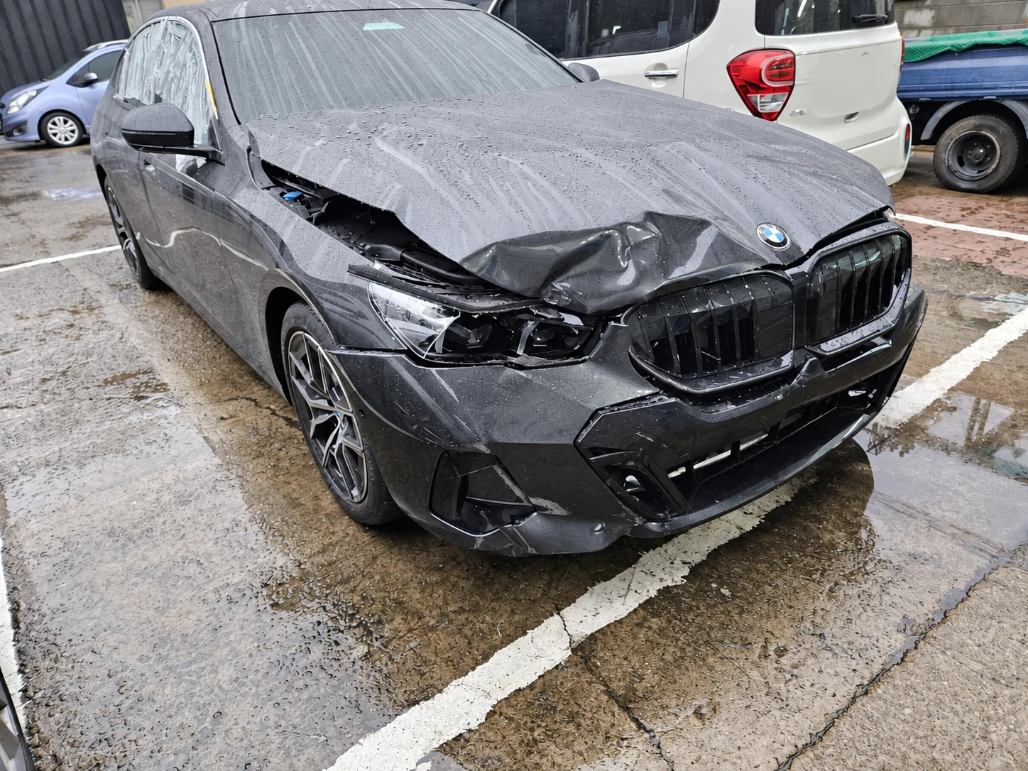 빗속에서 전면부가 심하게 파손된 BMW 세단